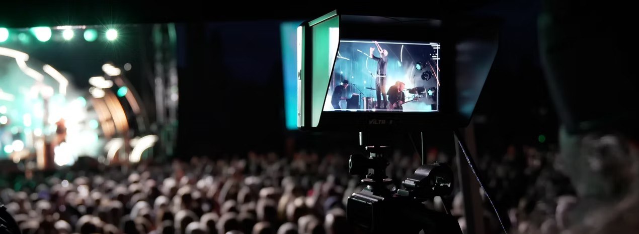 Kameraoperatør filmer et konsertpublikum og scenen gjennom kameraets monitor