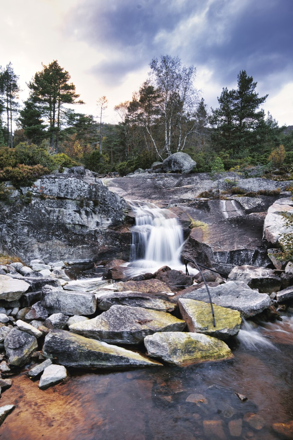 Foss i norsk skoglandskap under en dramatisk himmel